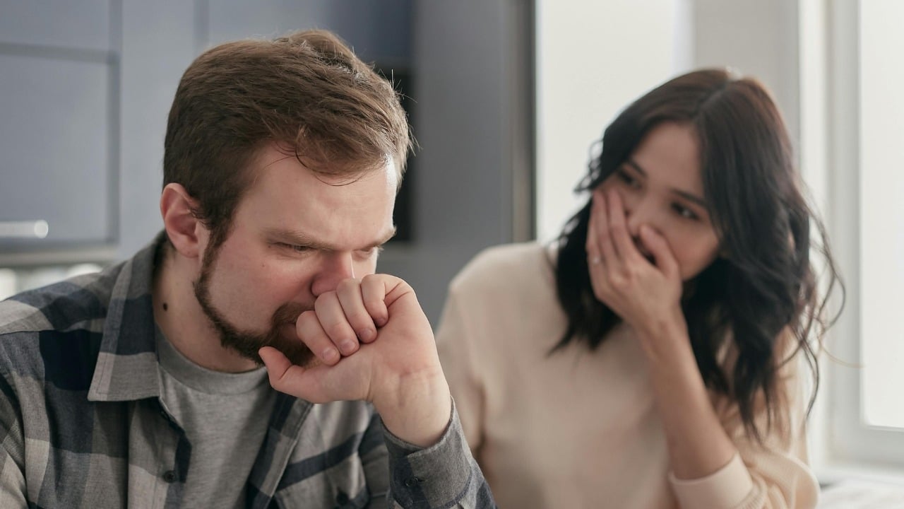 A woman looks toward a man who is gesturing with his hands during a conversation.