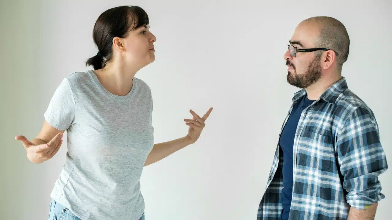 A woman in a grey shirt gestures with her hands while speaking to a man in a plaid shirt.