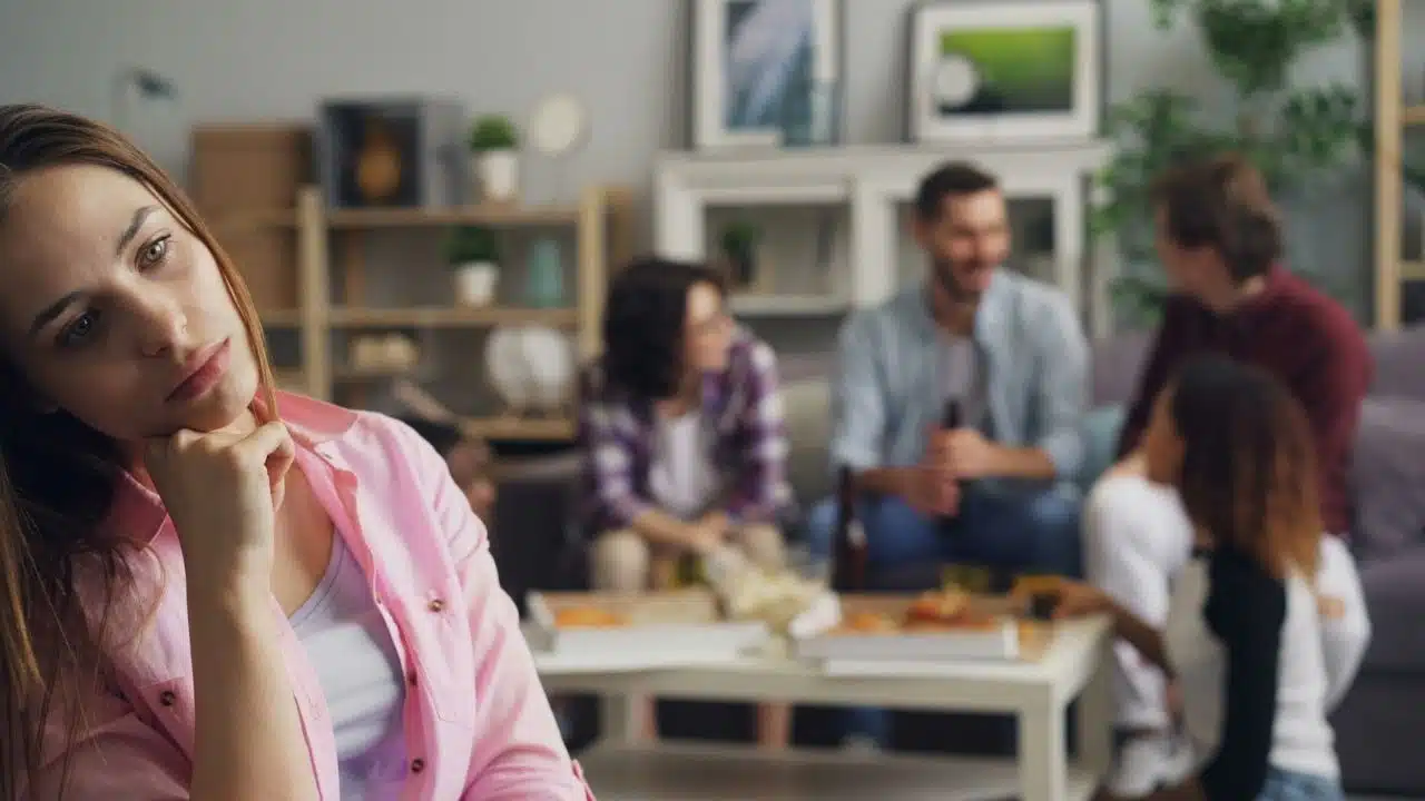 A woman in a pink shirt looks away while a group socializes in the background.