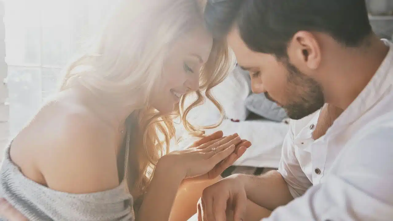 A couple leans their heads together while looking down at a ring on the woman's finger.