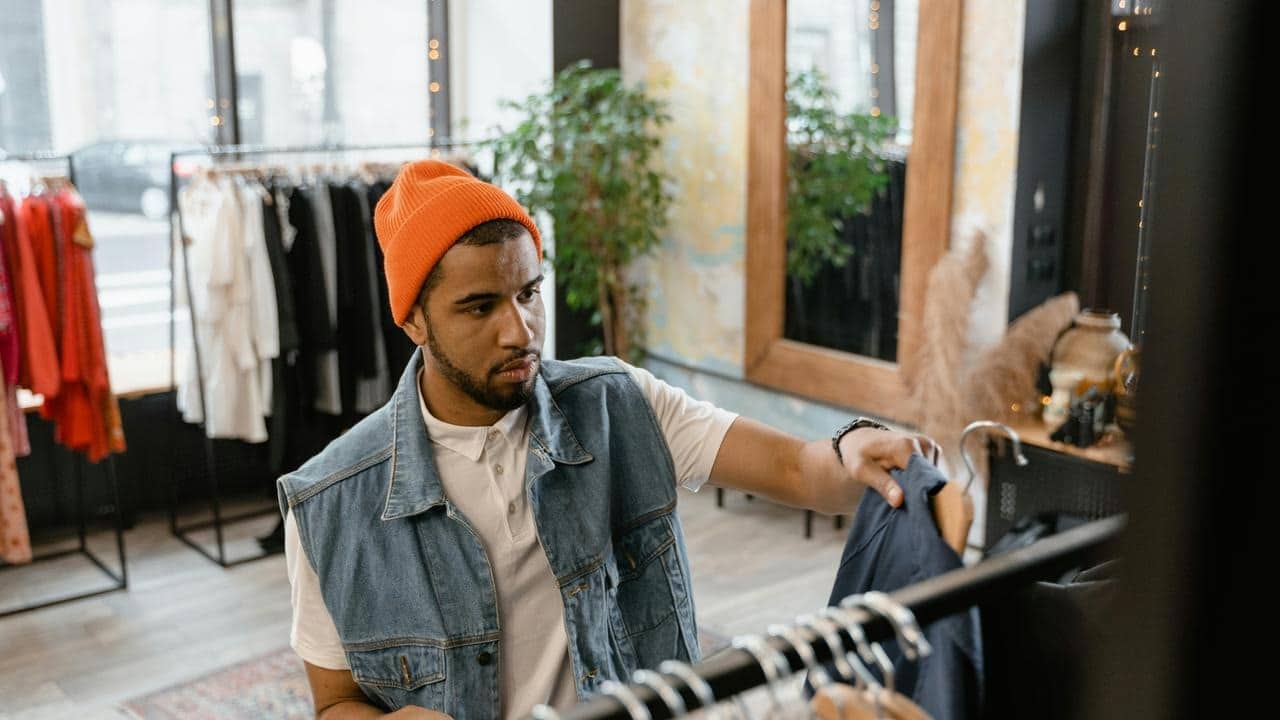 A man in a beanie browsing clothes in a shop.