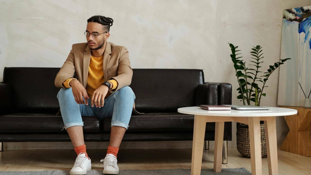 A man sitting on a couch looking down in a living room.