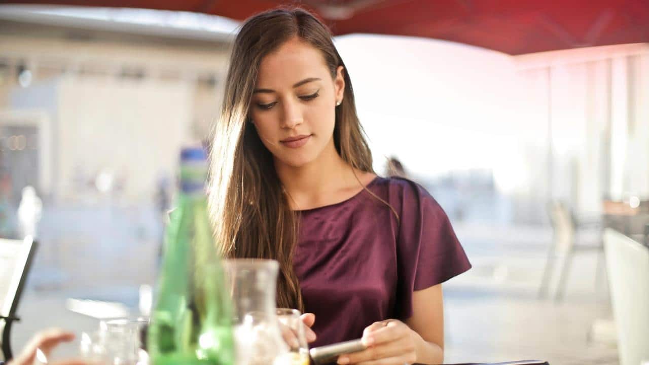 A woman sitting at an outdoor café table while looking at her phone.