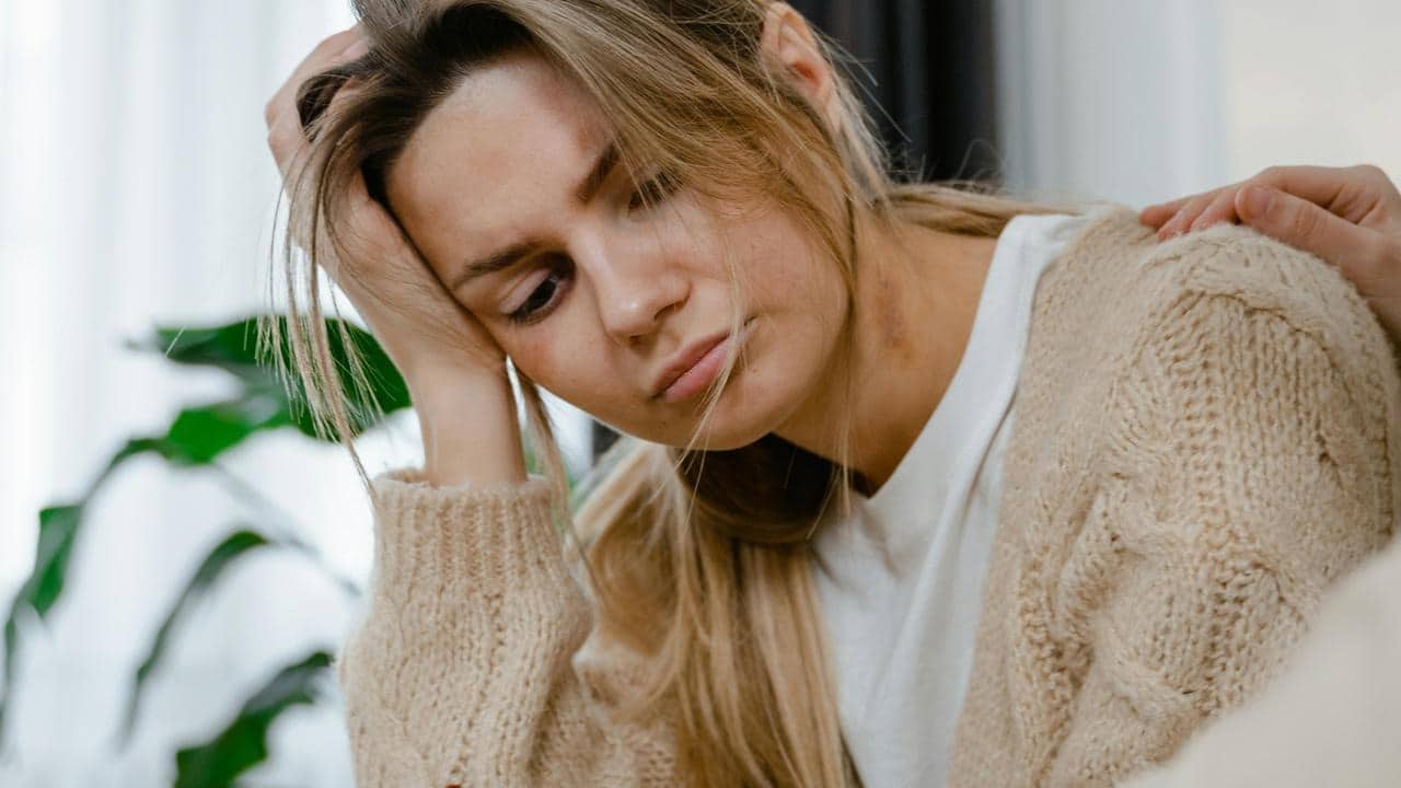 A sad woman resting her head on her hand while someone comforts her.
