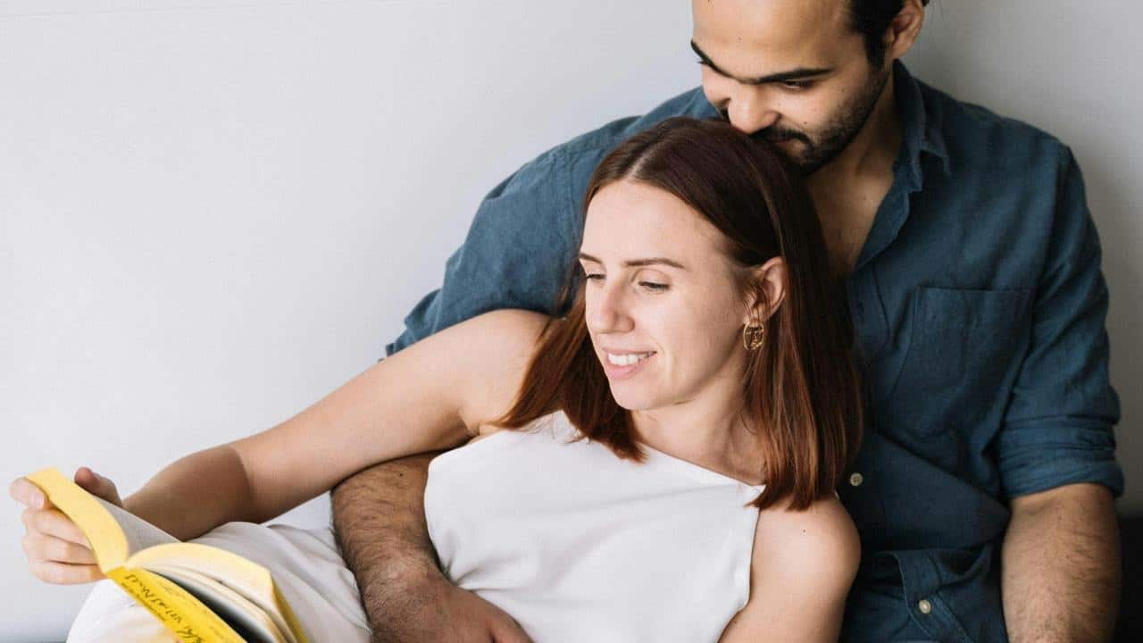 A couple sitting together while reading a book.