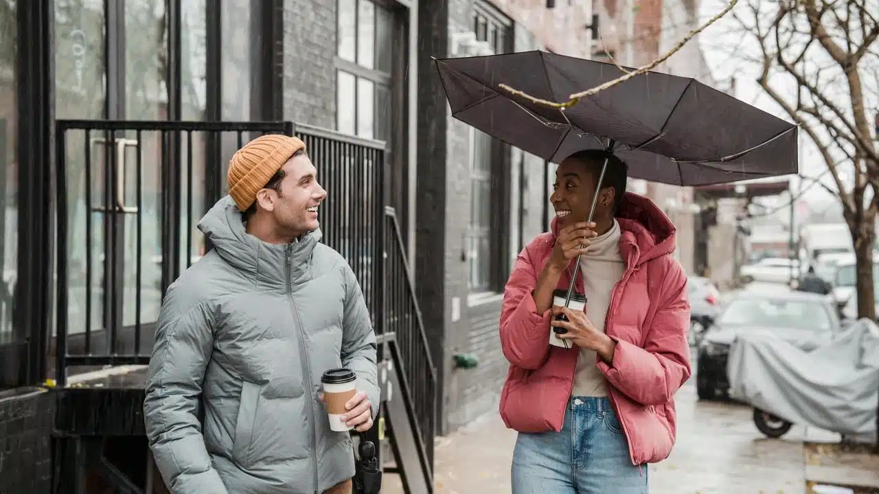 A man and woman walking on a rainy street while holding coffee and an umbrella.