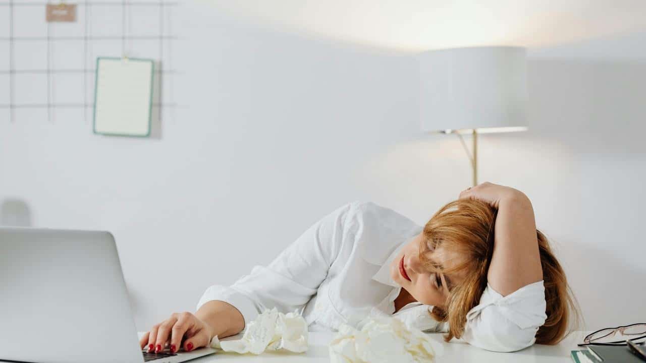 A tired woman resting her head on her arm while using a laptop at a desk.
