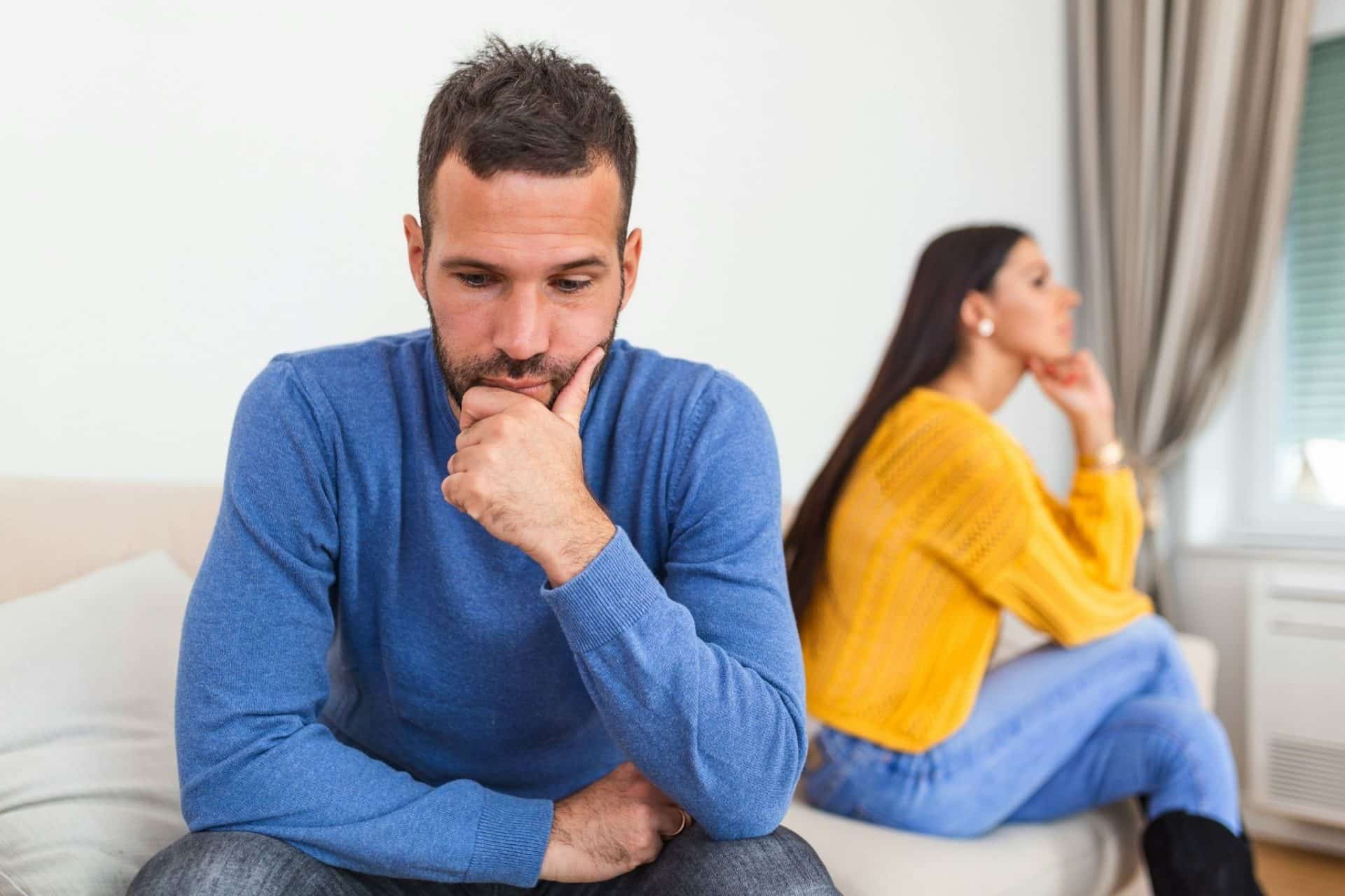 A man thinking deeply about something while a woman sits in the background.