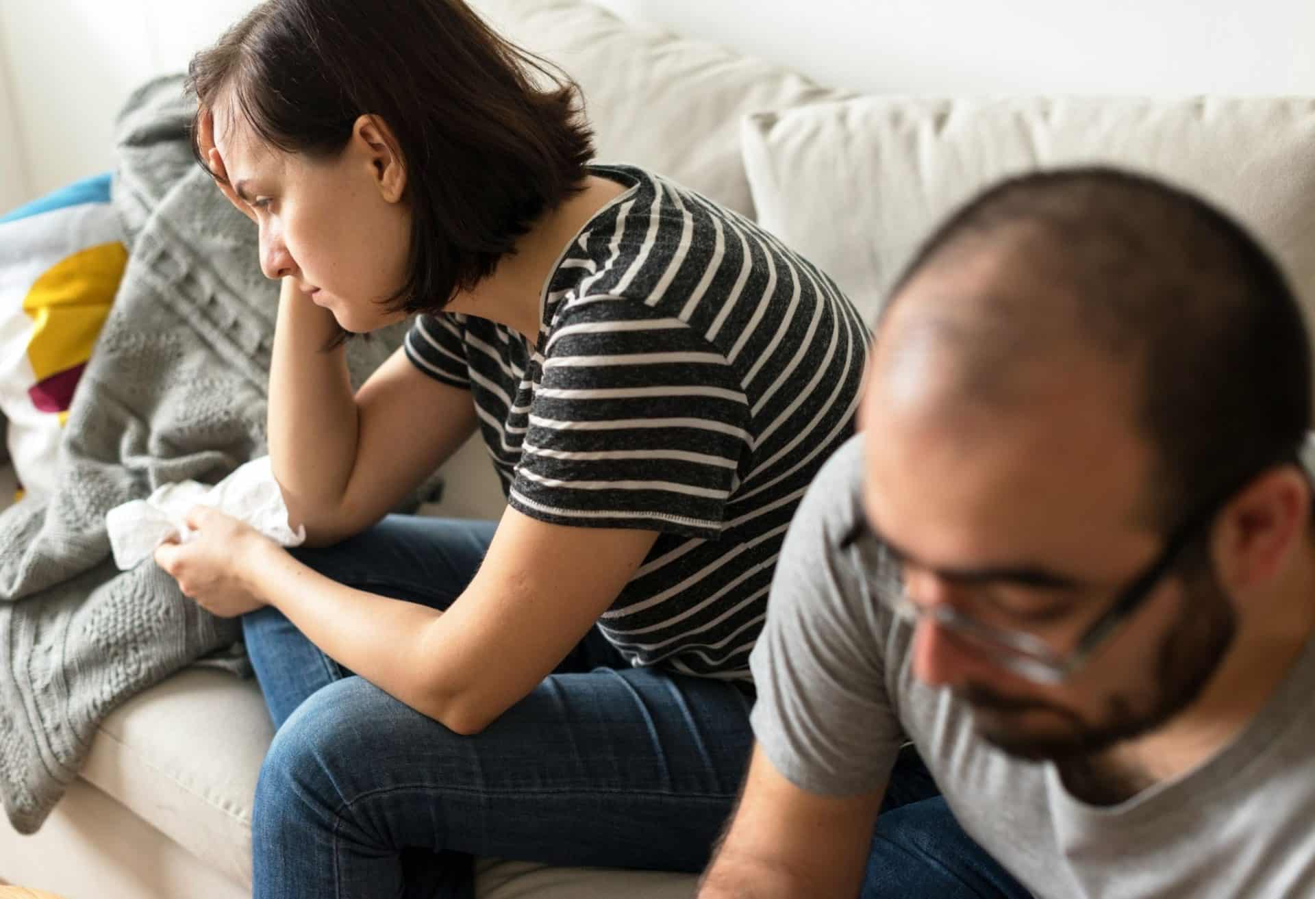 A woman appearing upset while she and a man sit on a couch.