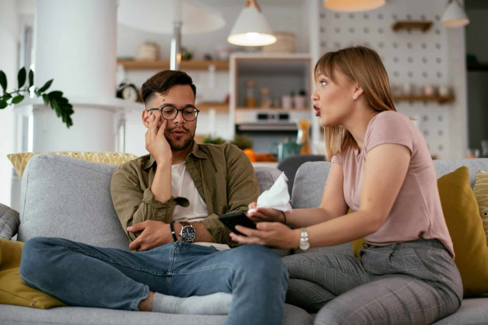 A woman confronting a man because she is irritated as they sit on a couch.