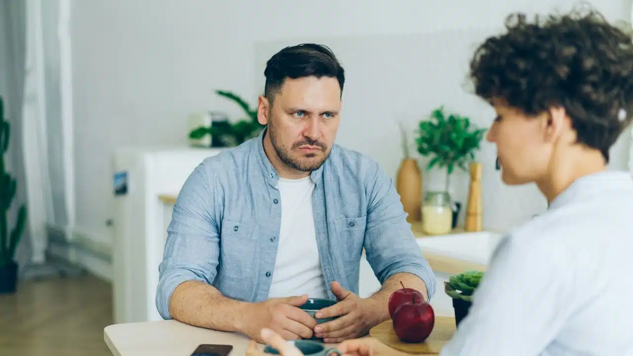 A man staring intensely at a woman as they have coffee while sitting at a table.
