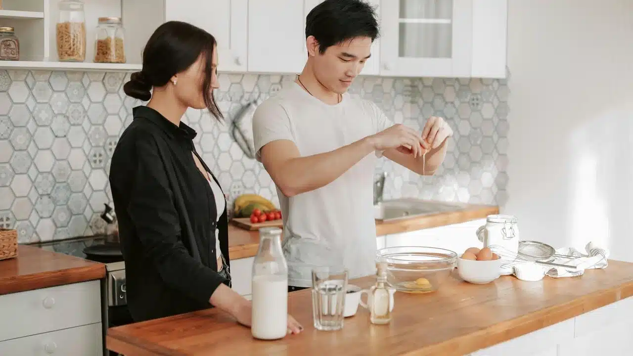 A couple preparing food in a kitchen, with one cracking eggs into a bowl.