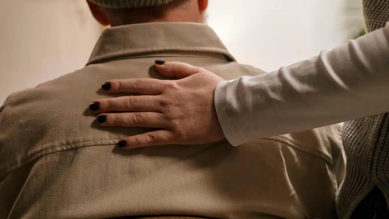 A person placing a comforting hand on another person’s shoulder.