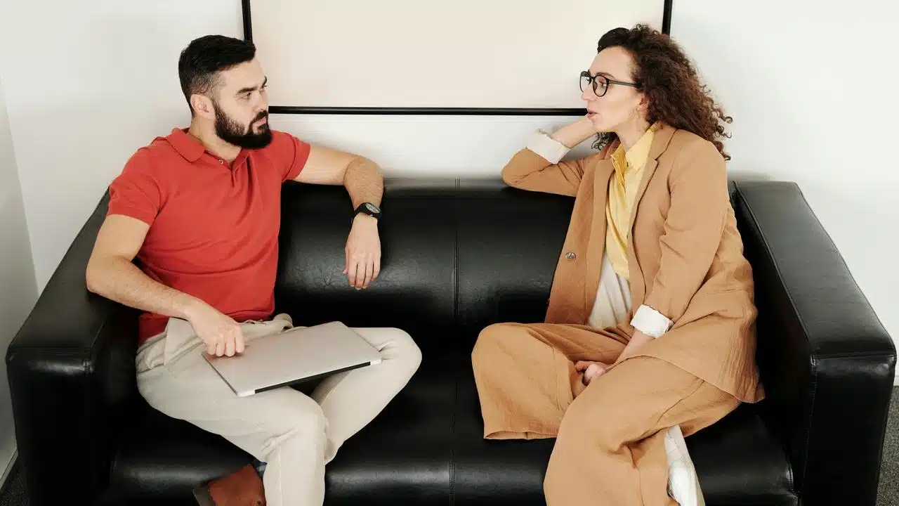 A man and woman sitting on a couch having a conversation.