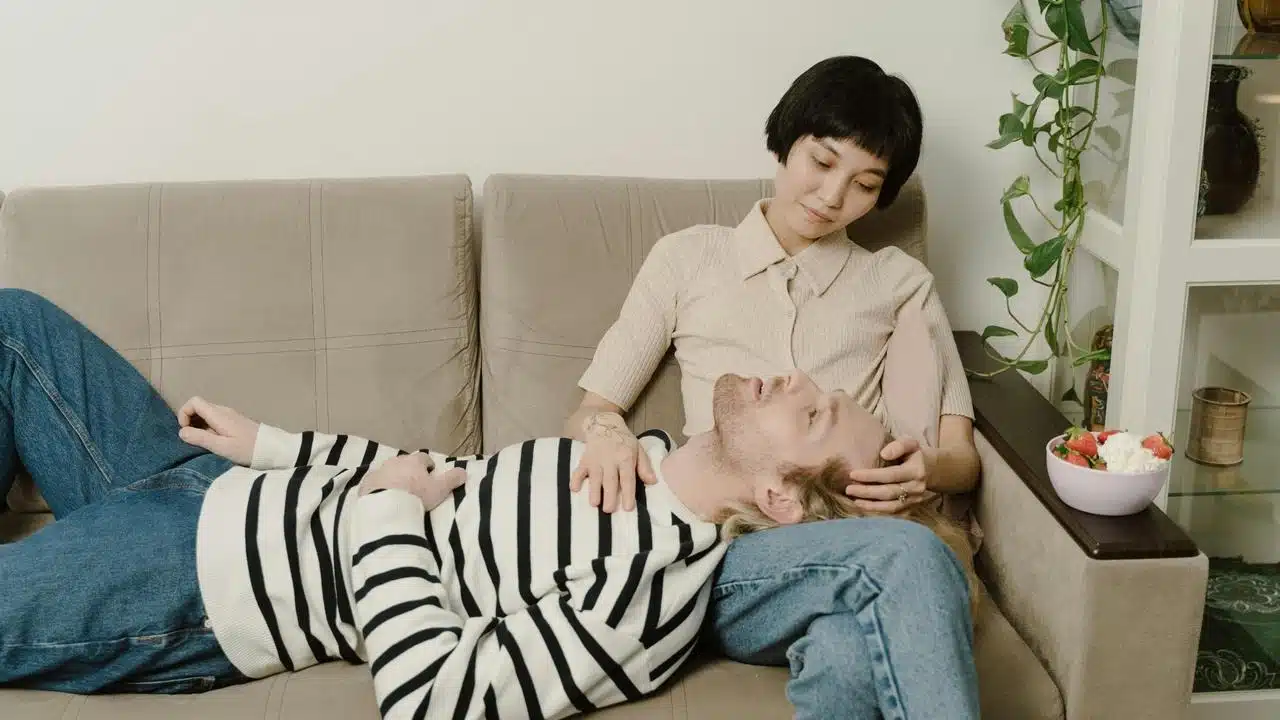 A couple relaxing on a couch, with one resting their head on the other's lap.