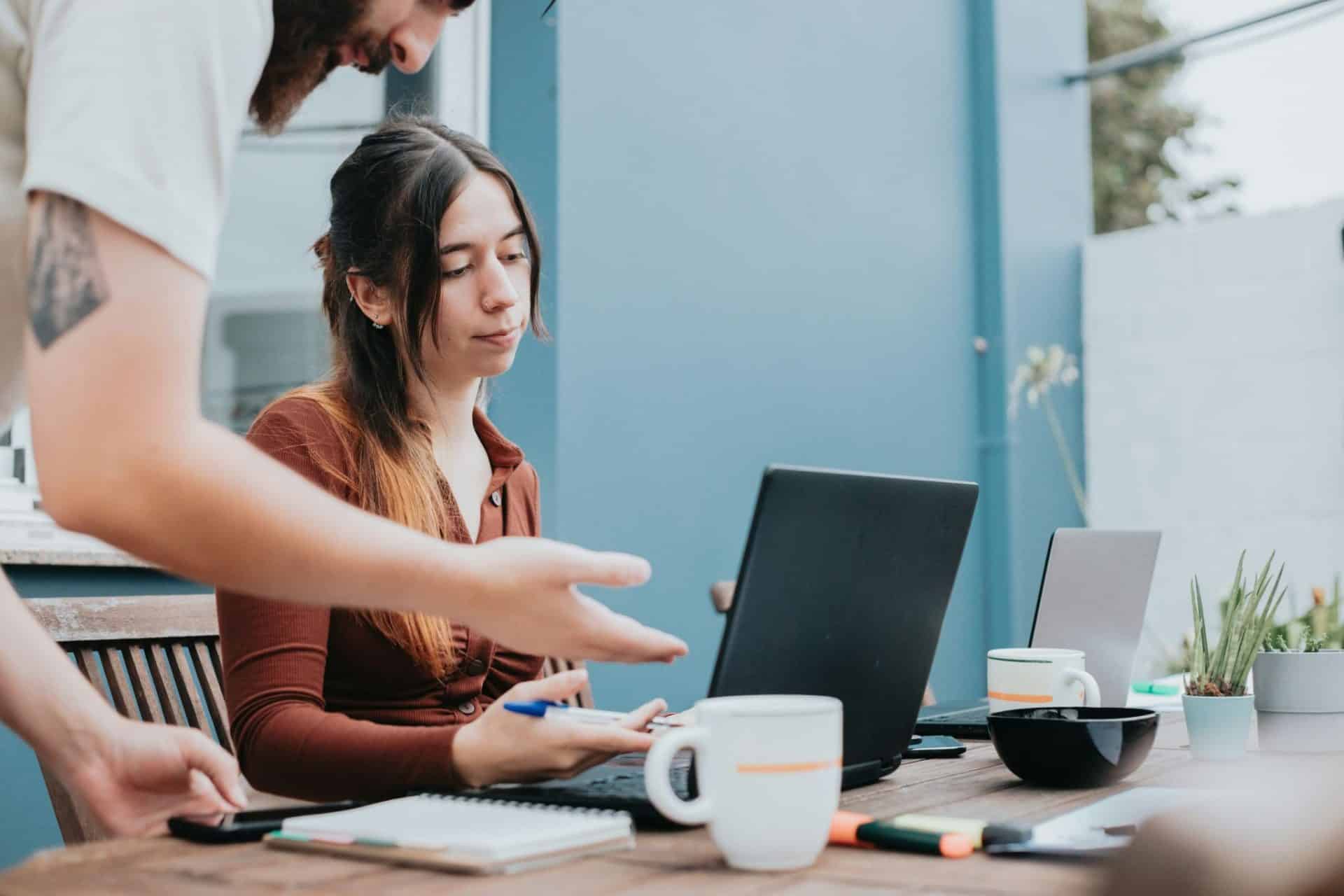 A woman looking indifferent as a man gestures at her laptop’s screen.