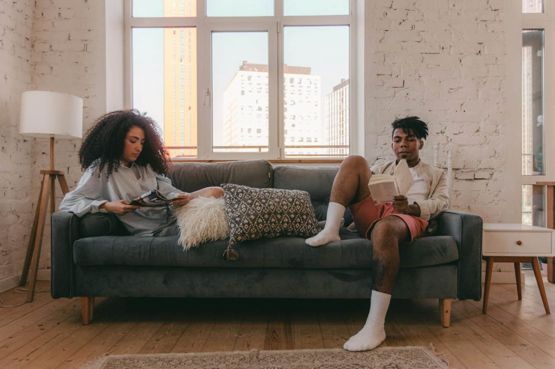 A couple sitting apart on the sofa while reading.