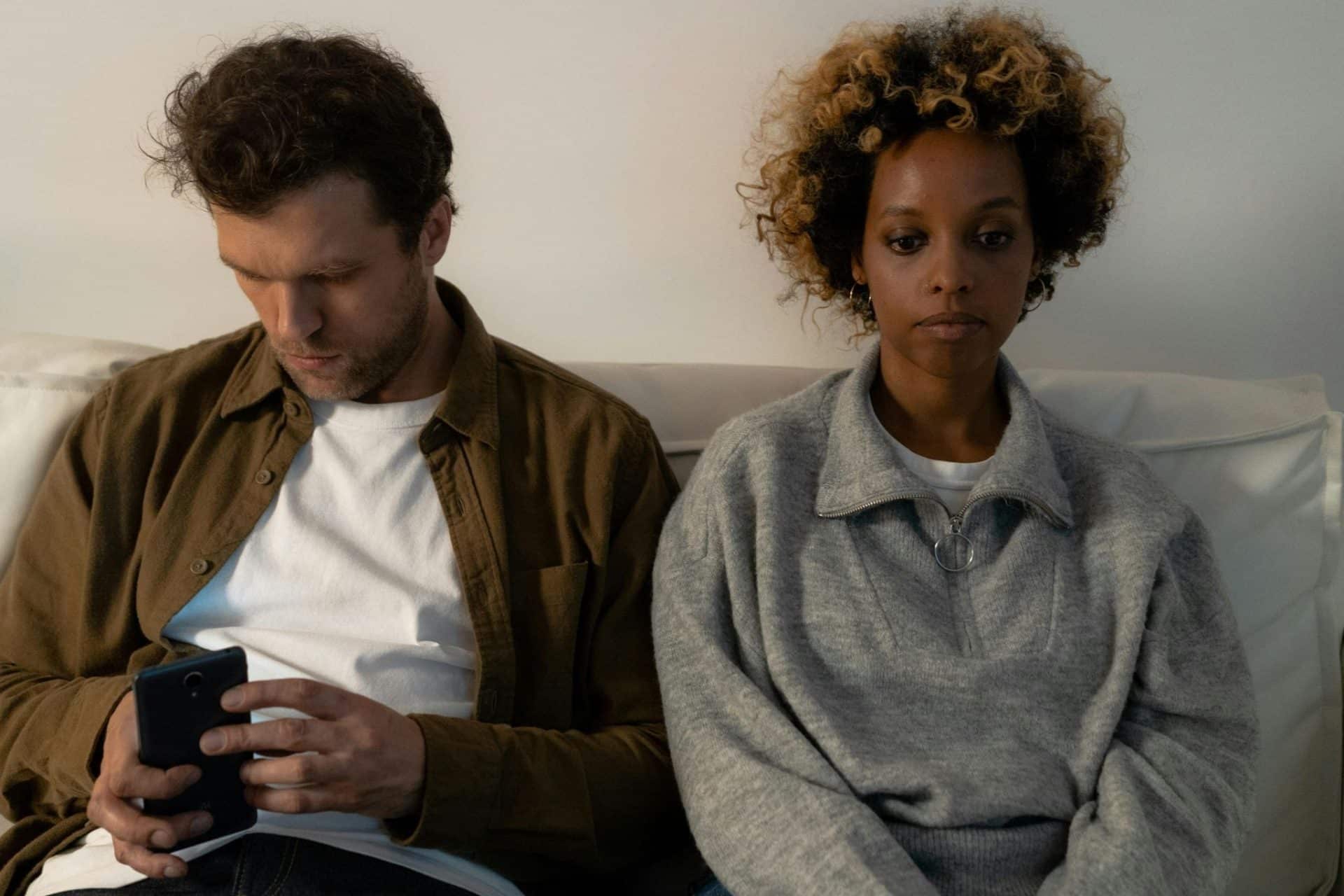 A man holding a phone sitting beside a sad woman.