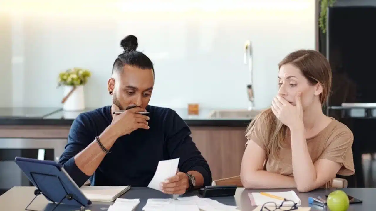 Couple reviewing bills with worried expressions at a kitchen table
