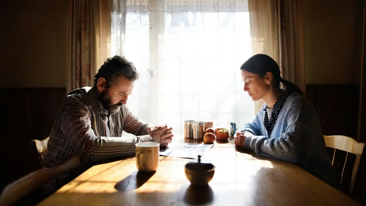 A man and woman sitting at a table and looking upset while refusing to talk to each other.