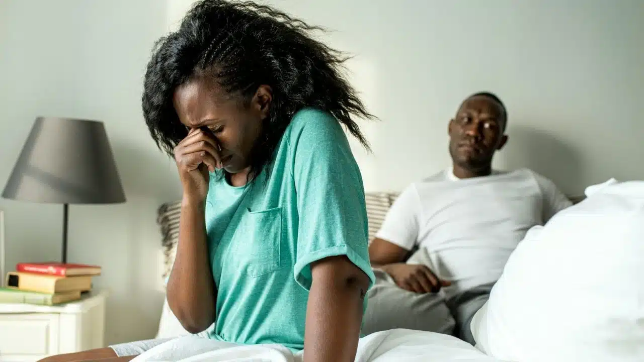 A woman in a green shirt rubs her eyes while a man watches from behind.