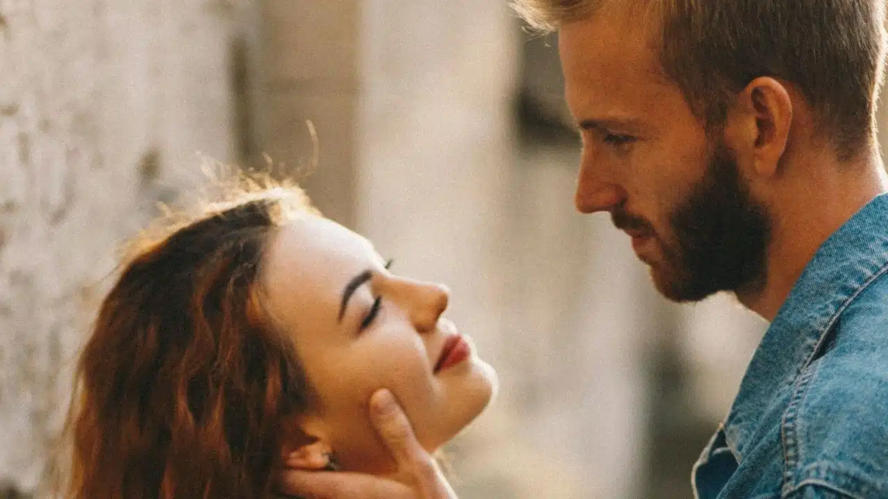 A man with a beard gazes at a woman while gently cupping her chin in his hand.