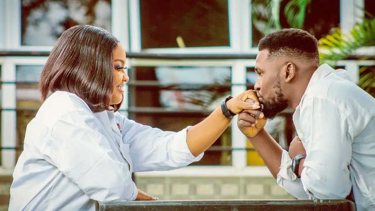 A man leans forward to kiss the hand of a woman who is smiling at him.