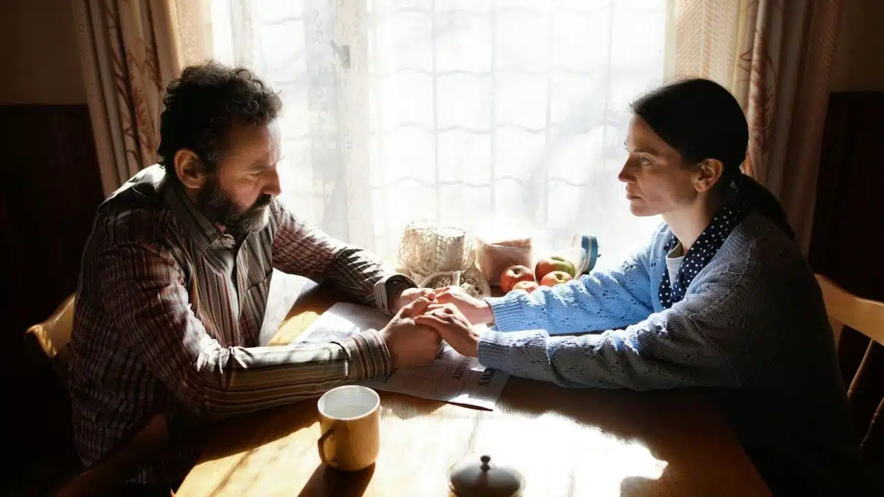 A man and a woman sit at a table, holding hands while looking at each other.