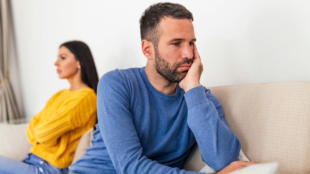 A man and a woman sitting separately on a couch after an argument.