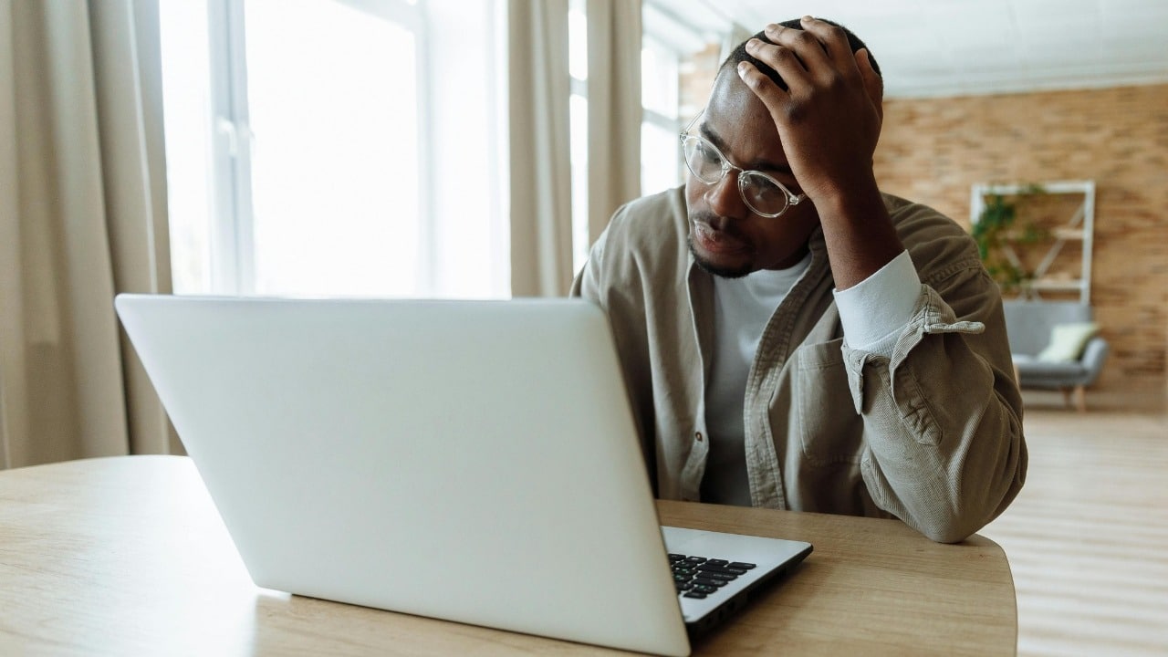 A man wearing glasses sits at a table and rests his head in his hand.