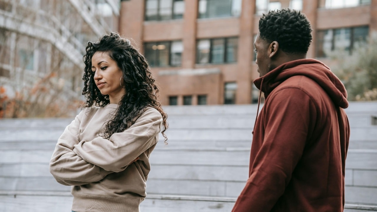 A woman looks at her phone while a man talks with his hands raised beside her.