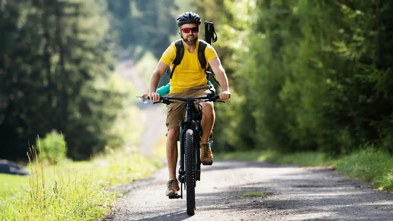 A man wearing a helmet and sunglasses rides a bicycle down a wooded path.
