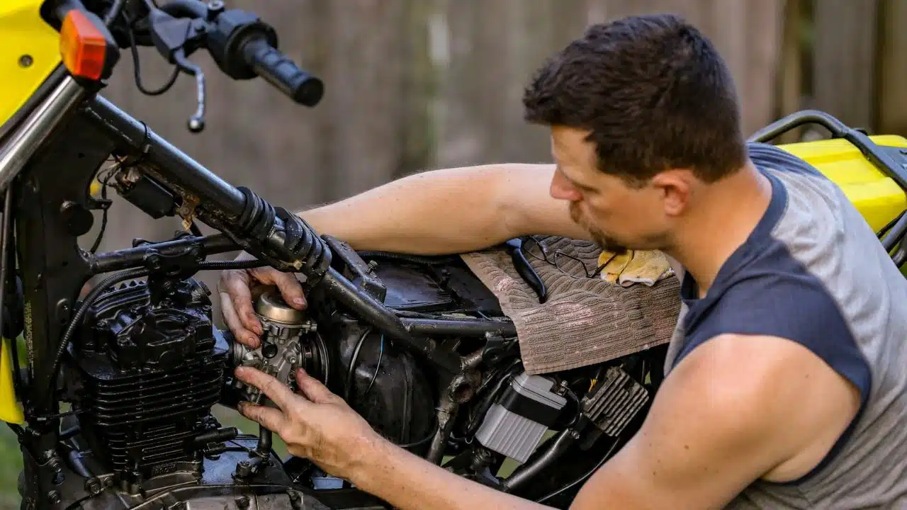 A man uses both hands to work on the engine components of a yellow motorcycle.