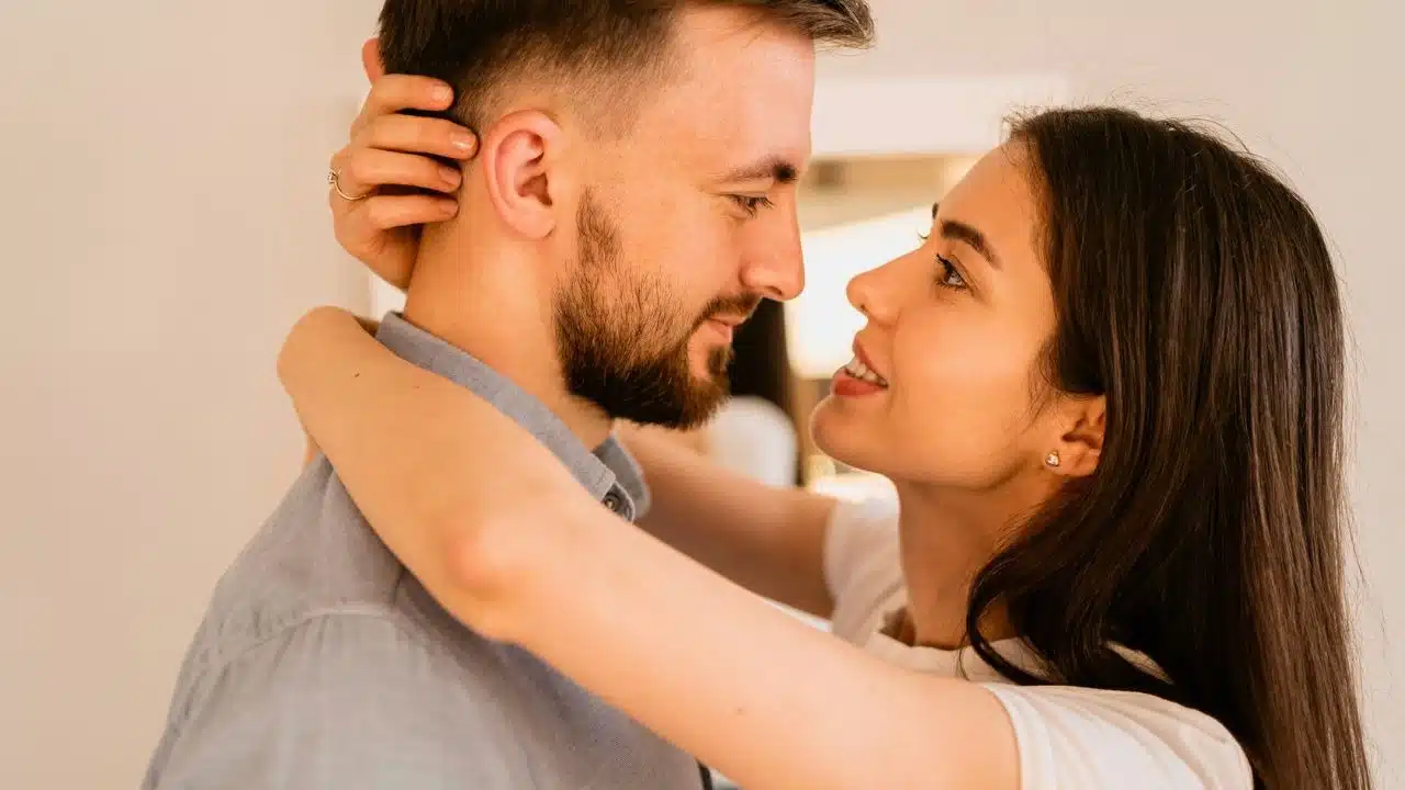 A woman with long dark hair smiles while embracing a man and holding his head.