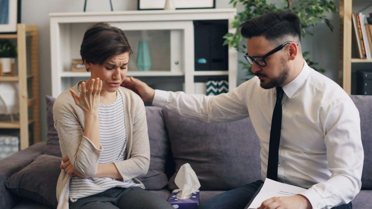 A man in a tie places his hand on the shoulder of a crying woman.