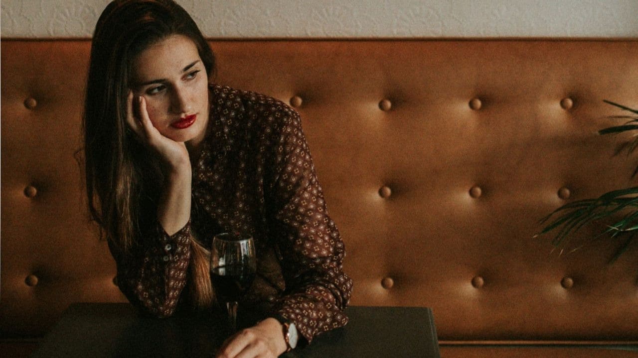 A woman with red lipstick leans her head on her hand next to a glass.