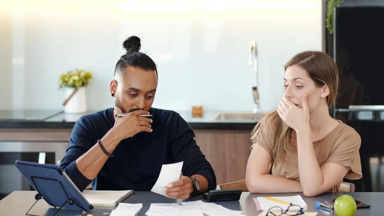 A man examines a small paper while a woman beside him covers her mouth with her hand.