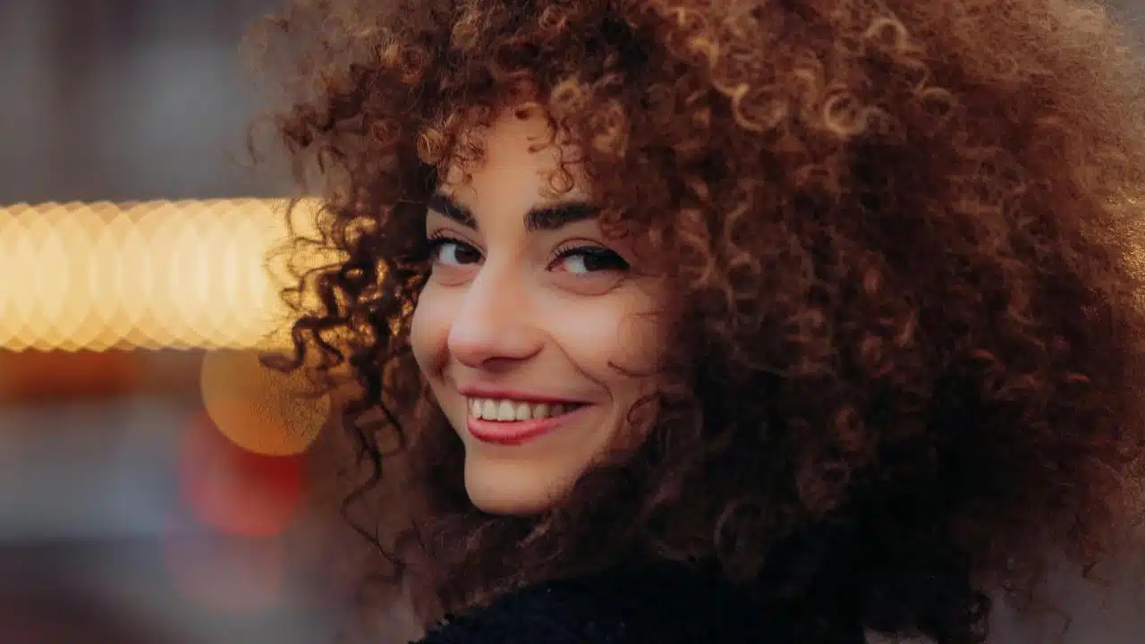 A woman with curly hair smiling at the camera outdoors.