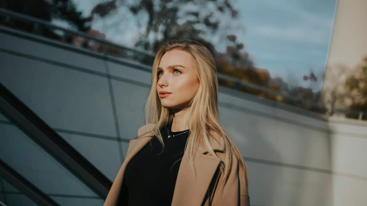 A woman standing outdoors, looking ahead in sunlight.