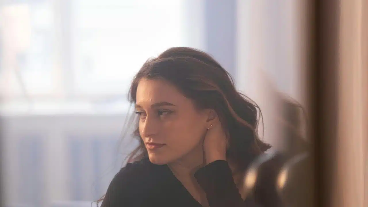 A woman looking to the side with her hand near her neck indoors.