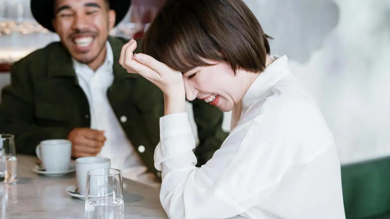A woman laughing with her hand on her forehead while sitting at a table.