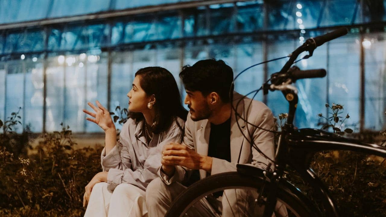 A couple sitting outdoors at night, talking beside a bicycle.