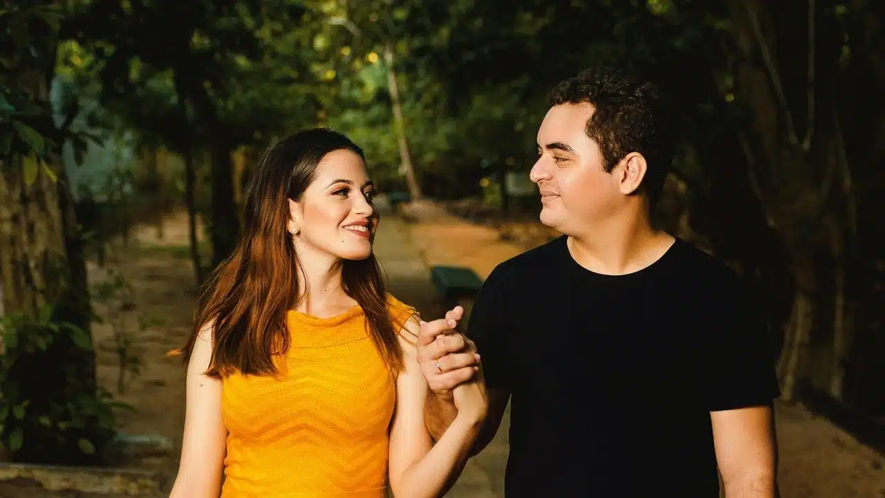 A couple holding hands and smiling at each other while walking outdoors.