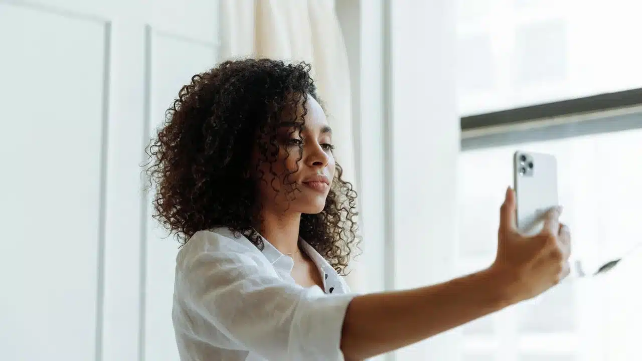 A woman holding a smartphone and taking a photo indoors.