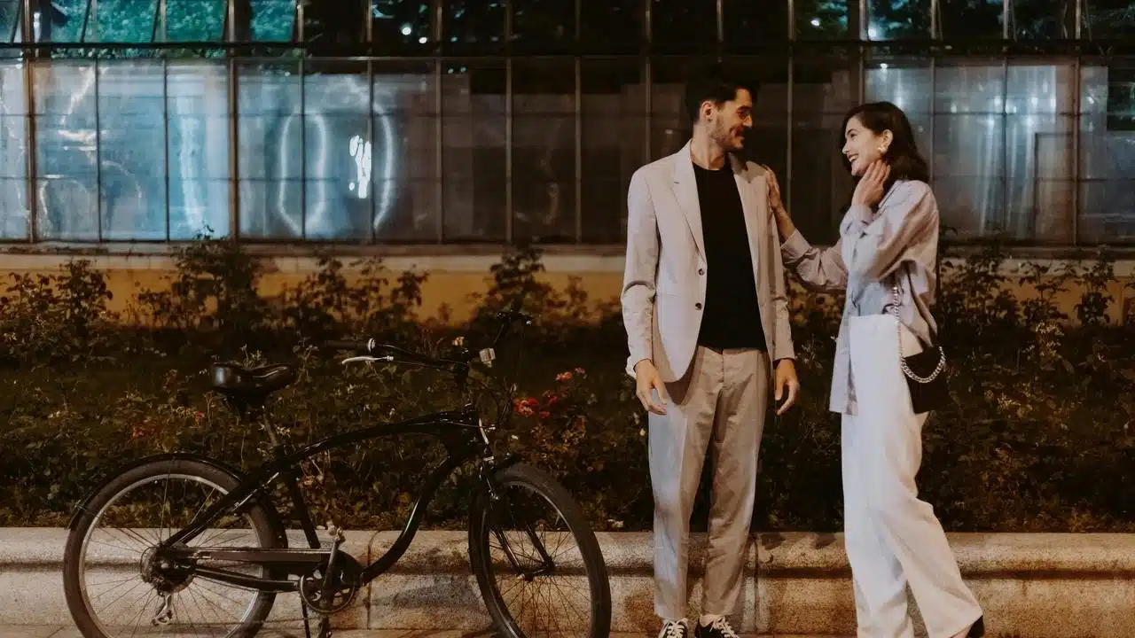 A couple standing outdoors at night, talking beside a bicycle.