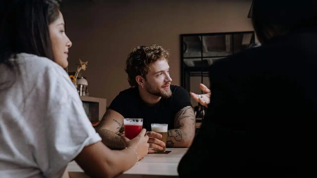 A group of people sitting at a table with drinks, talking and socializing indoors.