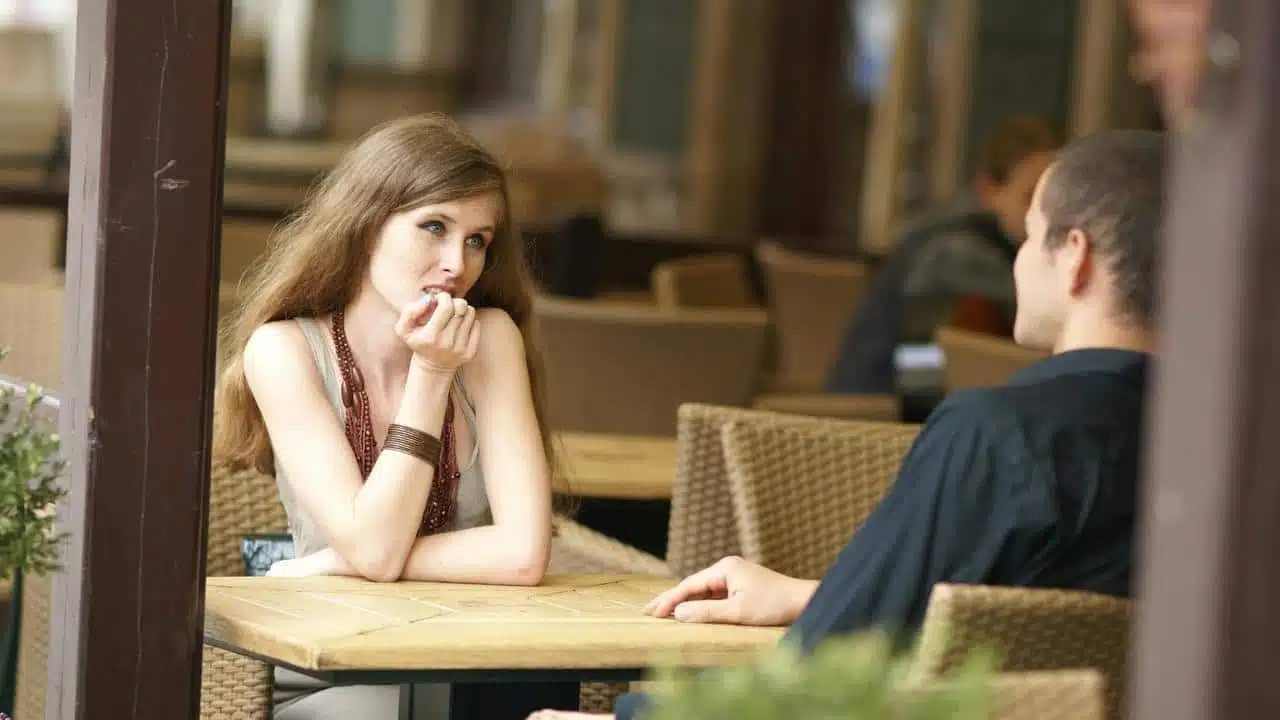 A woman resting her chin on her hand while talking to a man at a café table.