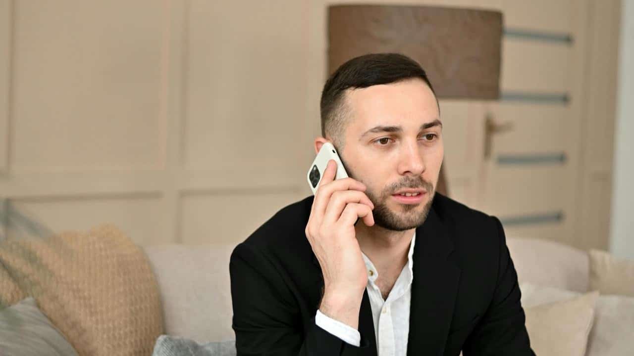 A man in a suit talking on his smartphone while sitting indoors.