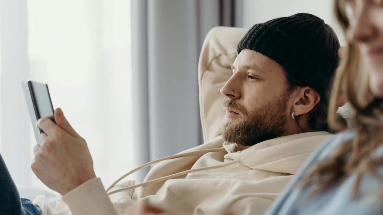 A man in a beanie lying down while looking at his smartphone.