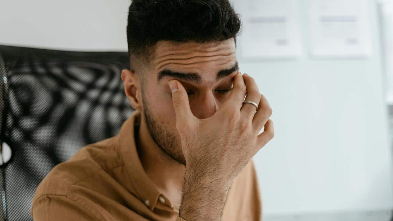 A man covering his face with his hand, appearing tired or stressed.